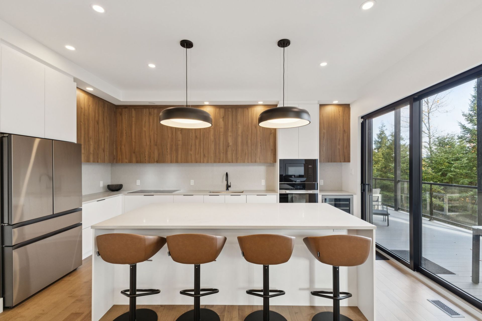 Cuisine moderne avec îlot central, tabourets de bar marron et portes coulissantes en verre donnant sur une terrasse extérieure.