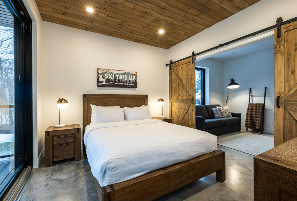 Chambre avec un cadre de lit en bois, des portes de grange et un petit coin salon.