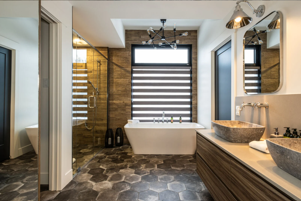 Salle de bains moderne avec baignoire, lavabos en pierre et sol carrelé à motifs.