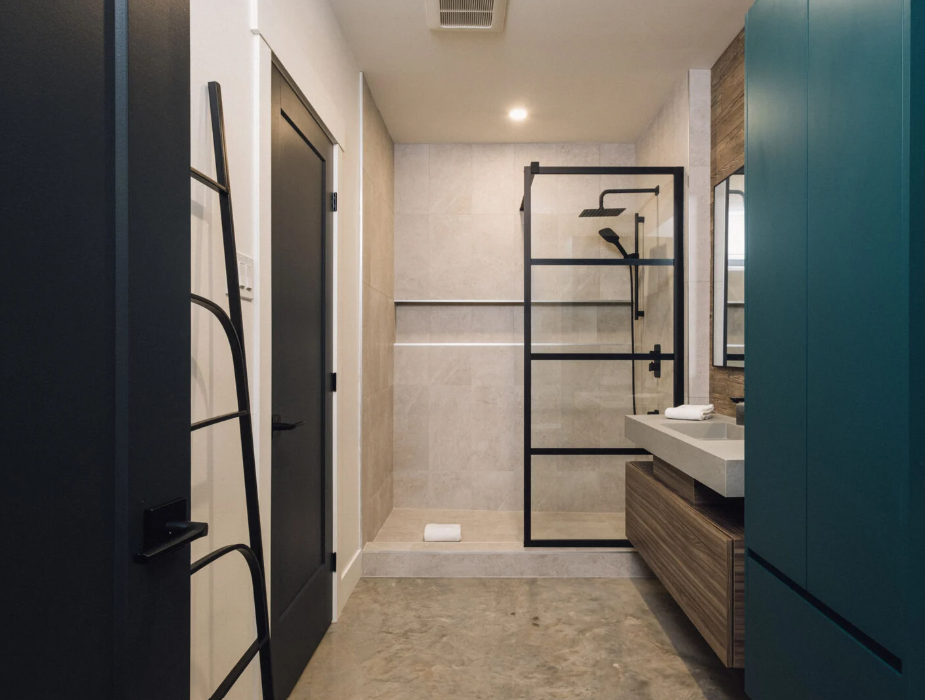 Salle de bains avec porte de douche à cadre noir, murs carrelés gris et meuble-lavabo en bois.