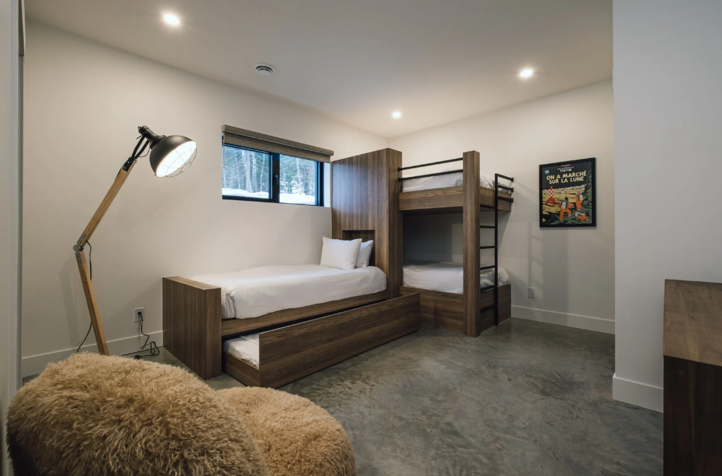 Chambre avec lits superposés, un lit gigogne, un lampadaire, un pouf et une petite fenêtre.