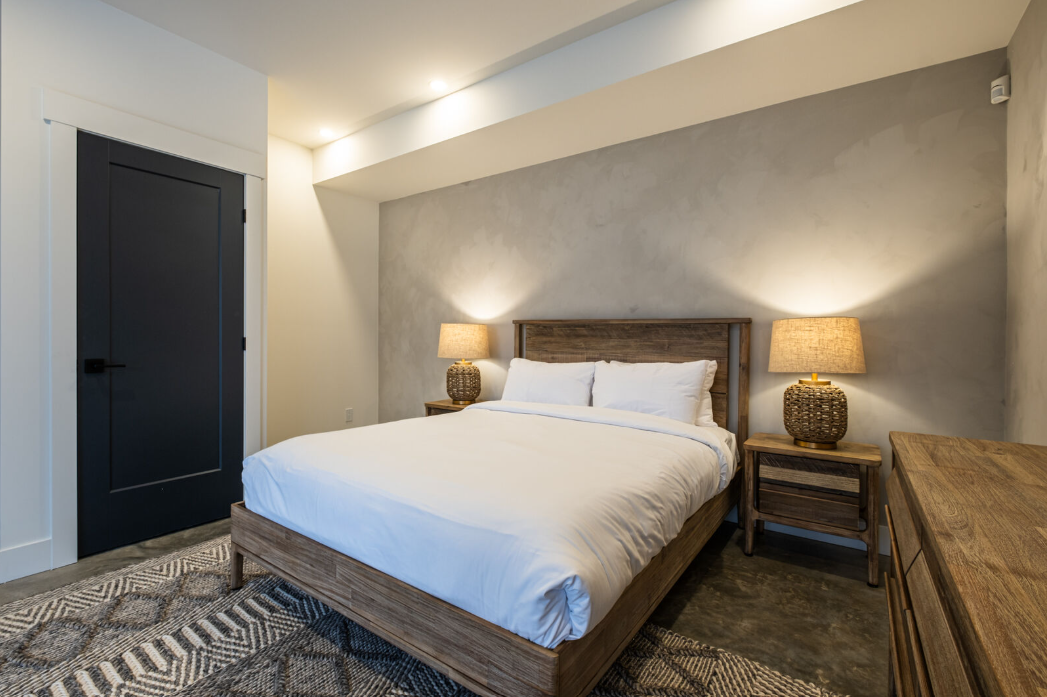 Chambre avec lit, tables de chevet, lampes, porte sombre et tapis texturé.