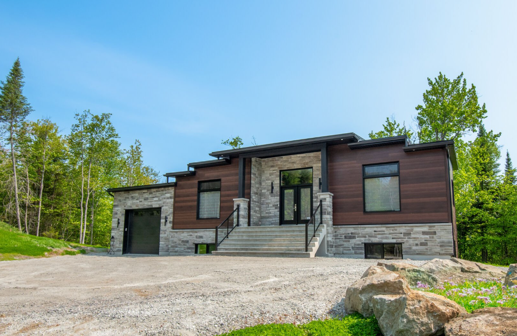 Maison moderne avec extérieur en pierre et en bois, sous un ciel bleu.