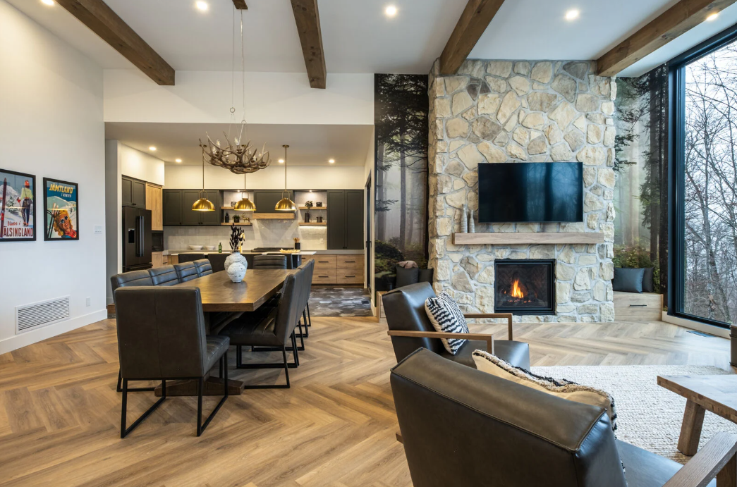Espace de vie ouvert comprenant un coin repas, une cuisine et une cheminée. Cheminée en pierre avec télévision fixée au mur.