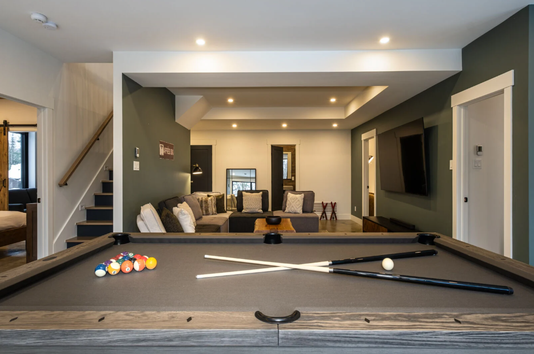 Table de billard dans une salle de jeux avec canapé, télévision et escalier.