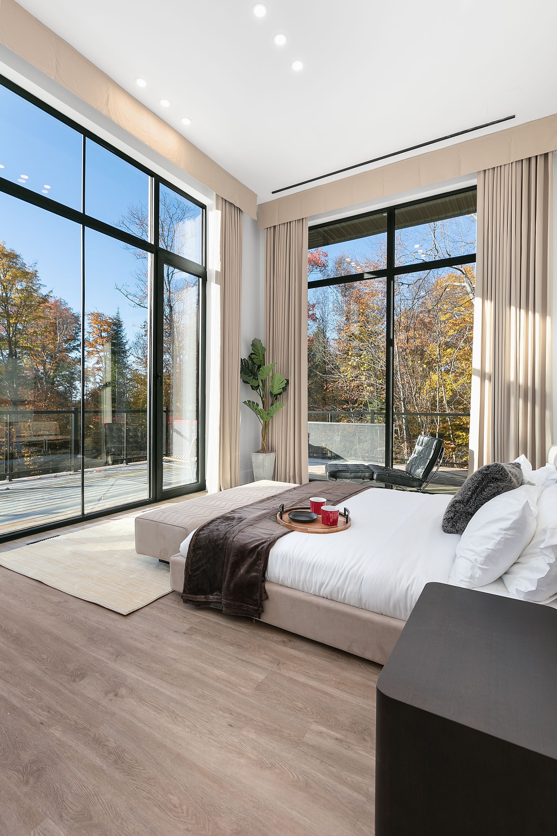 Chambre avec de grandes fenêtres, tons neutres, lit à tablette, vue sur les arbres, lumière naturelle.