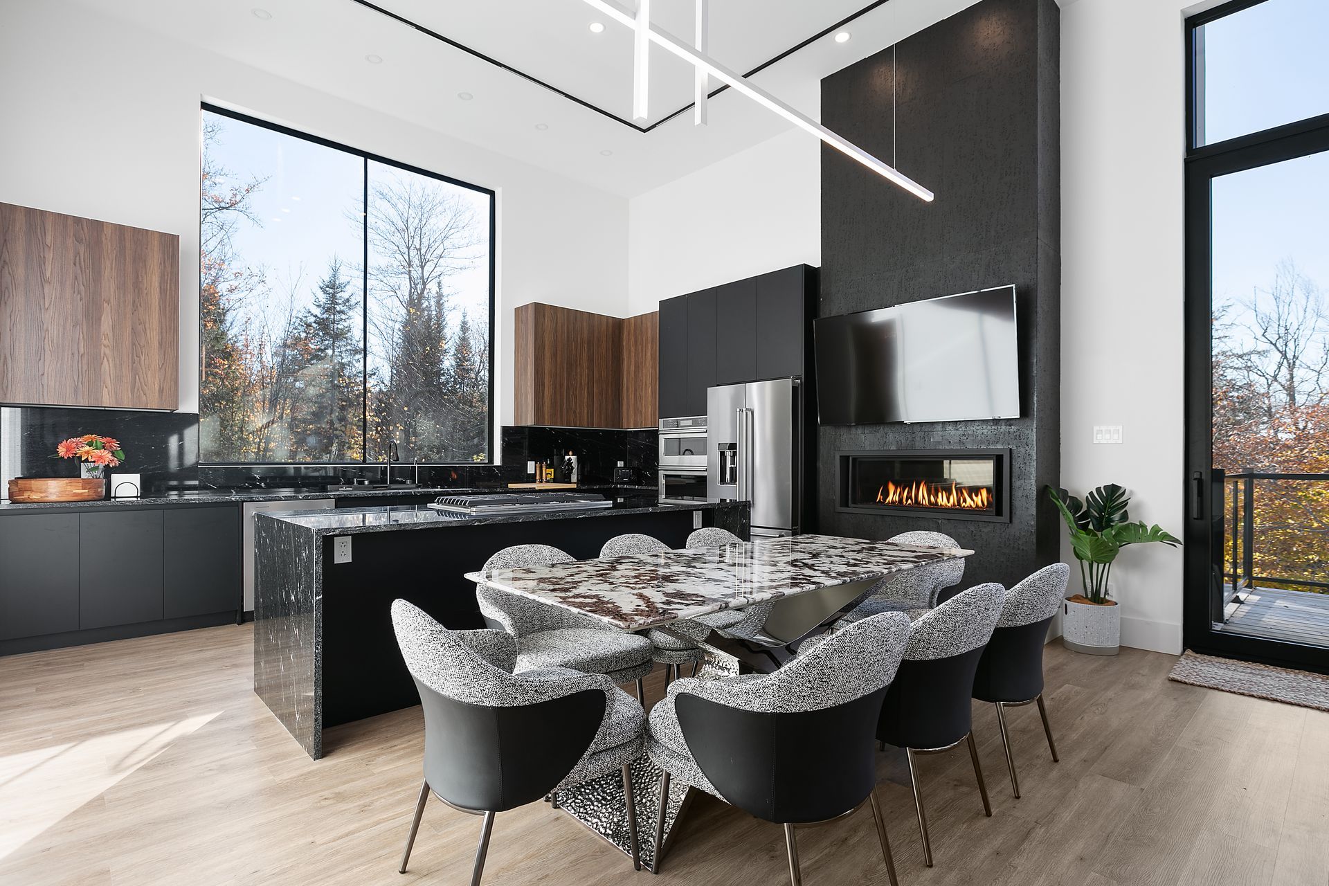 Cuisine et salle à manger modernes avec îlot central noir, cheminée, grandes fenêtres et chaises design.