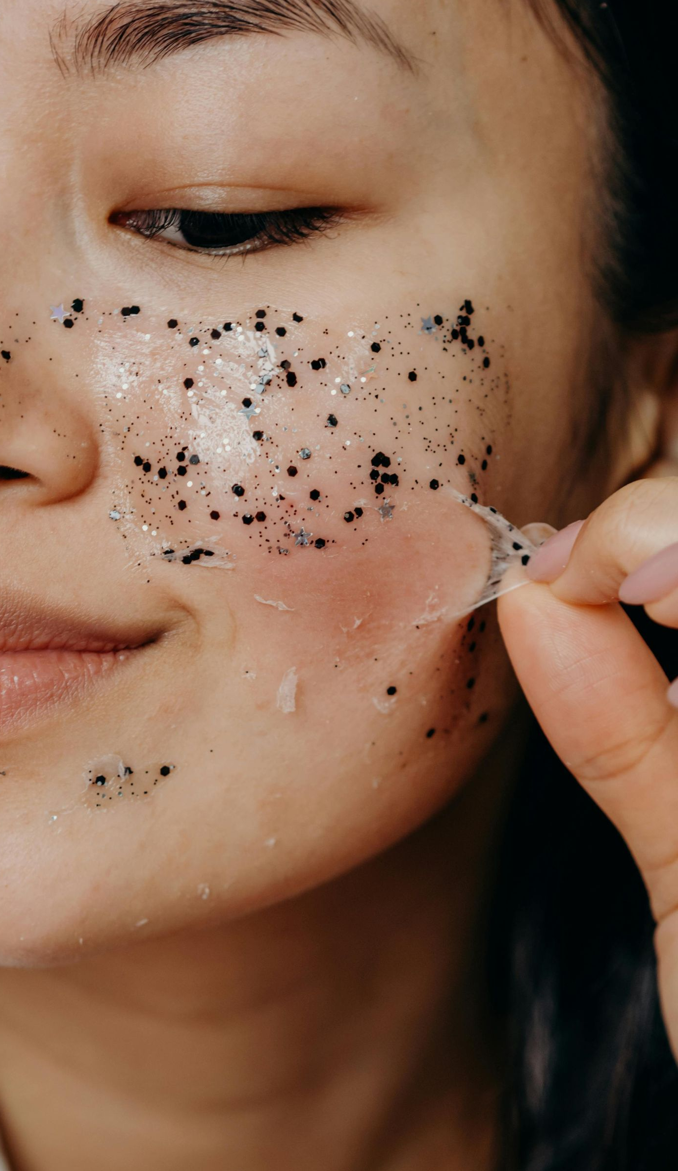 Woman peeling a facial mask from her cheek. The mask has black particles.