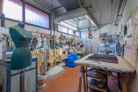 Un piccolo laboratorio disordinato con un manichino da sarto verde, un grande tavolo da lavoro in legno e attrezzi appesi alle pareti.