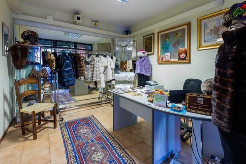 L'interno di una boutique con pellicce appese a grucce, una scrivania, una sedia di legno e un tappeto a motivi geometrici su un pavimento piastrellato.