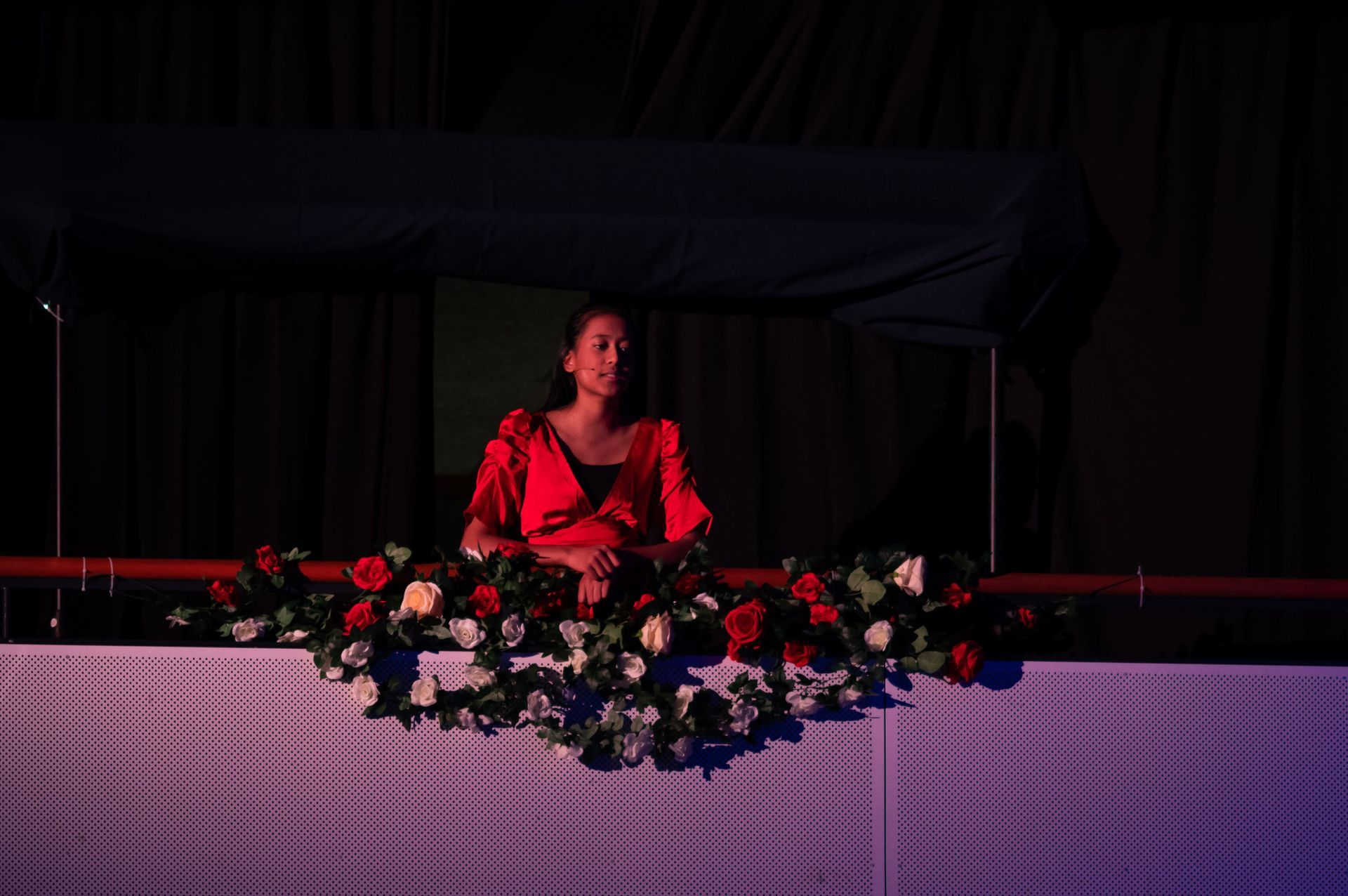 Een vrouw in een rode jurk staat op een balustrade met bloemen.