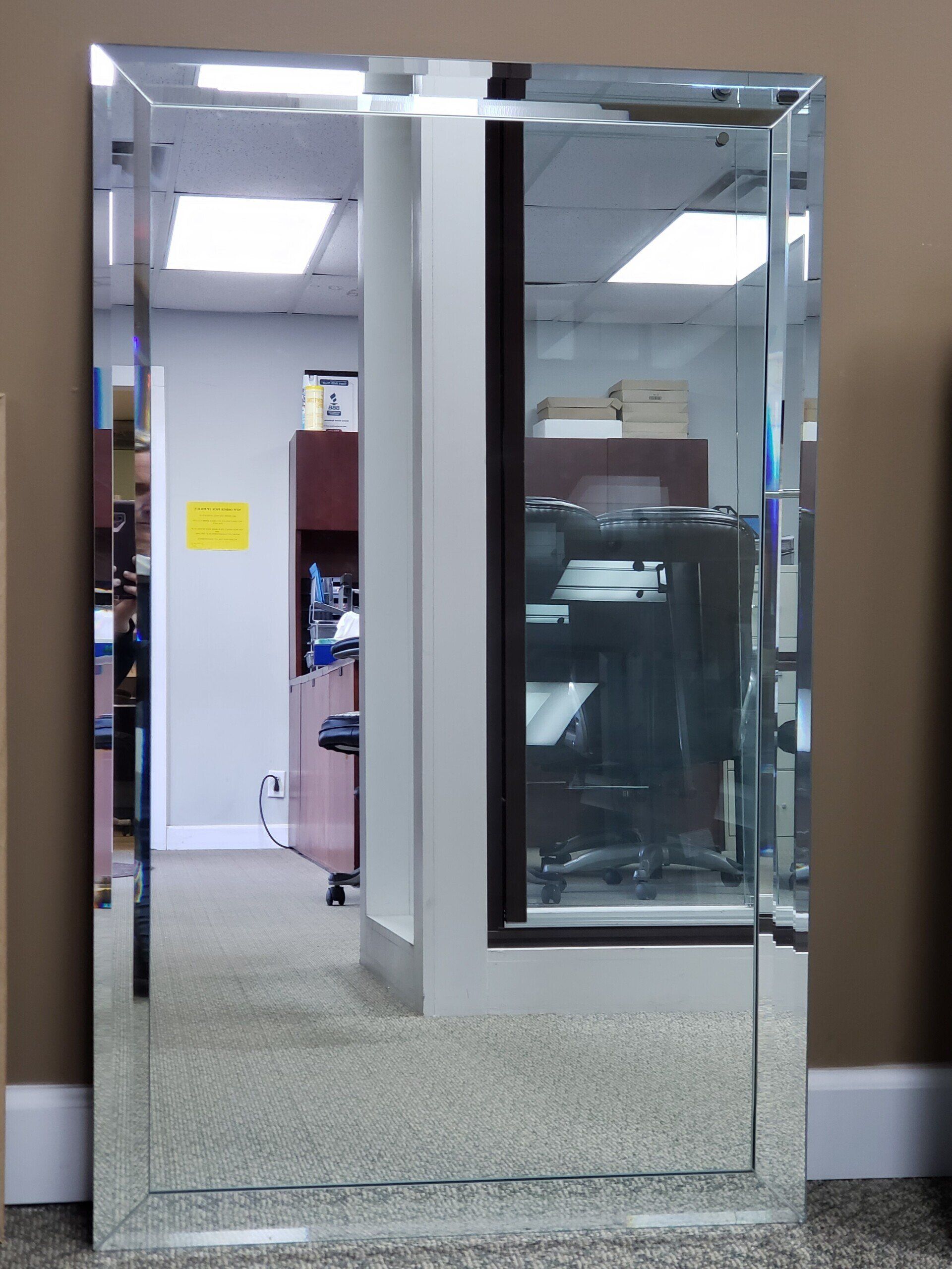 Full-length rectangular beveled mirror reflecting an office.
