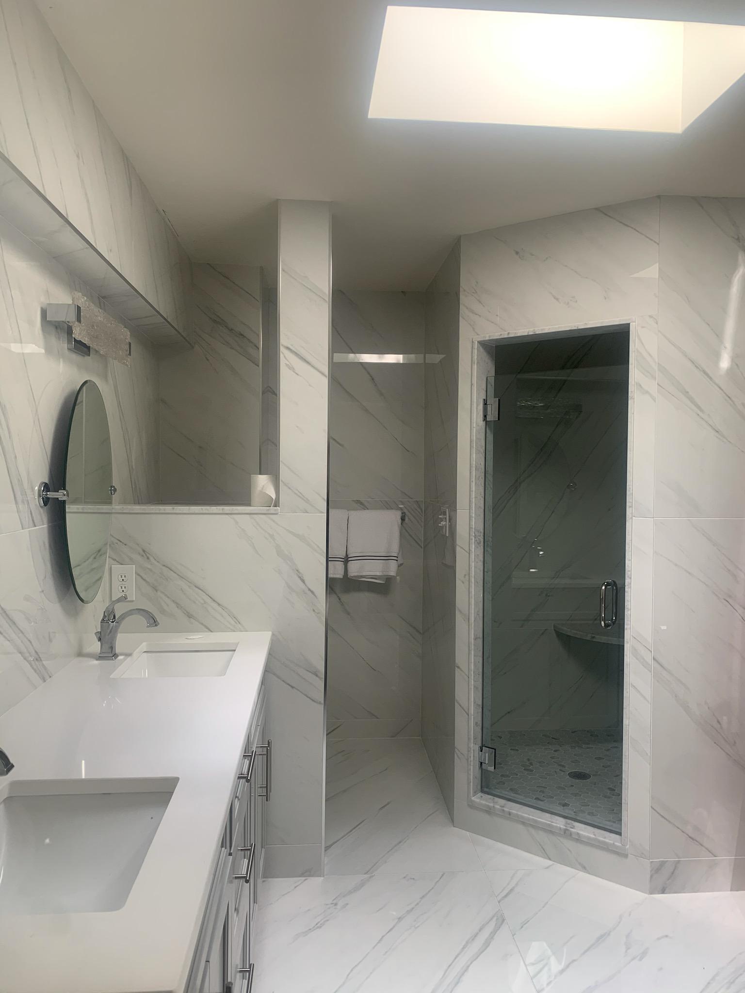Modern bathroom with white marble tile, glass shower, double sink vanity, and a skylight.