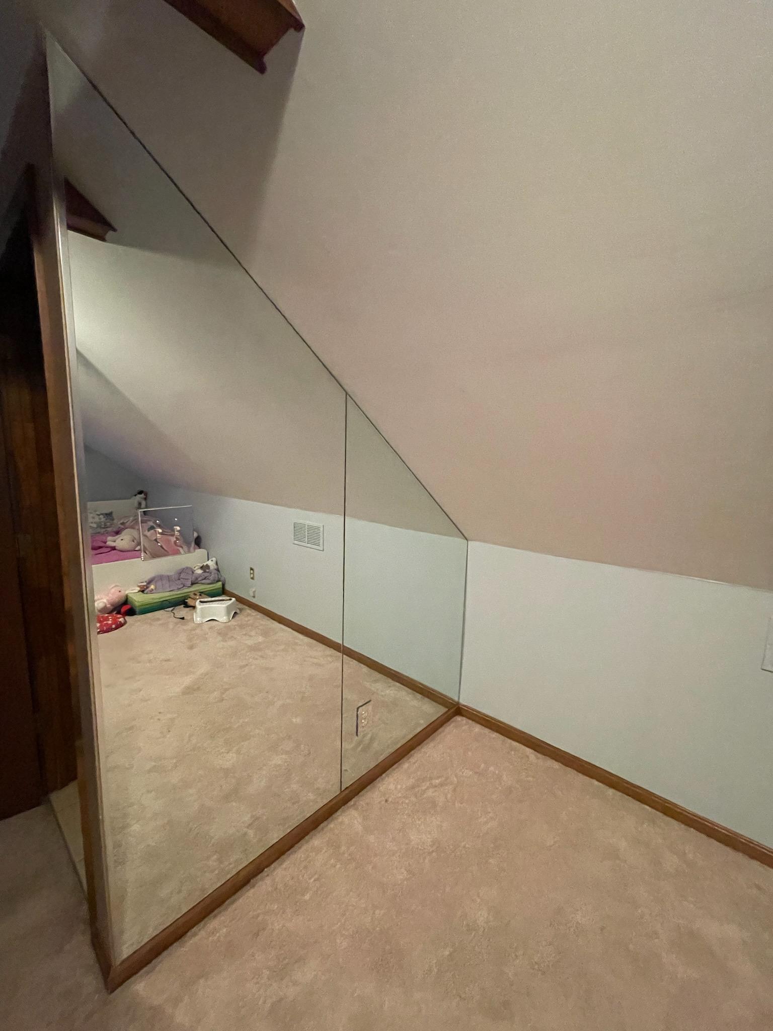 Mirror on slanted wall in room with tan carpet.