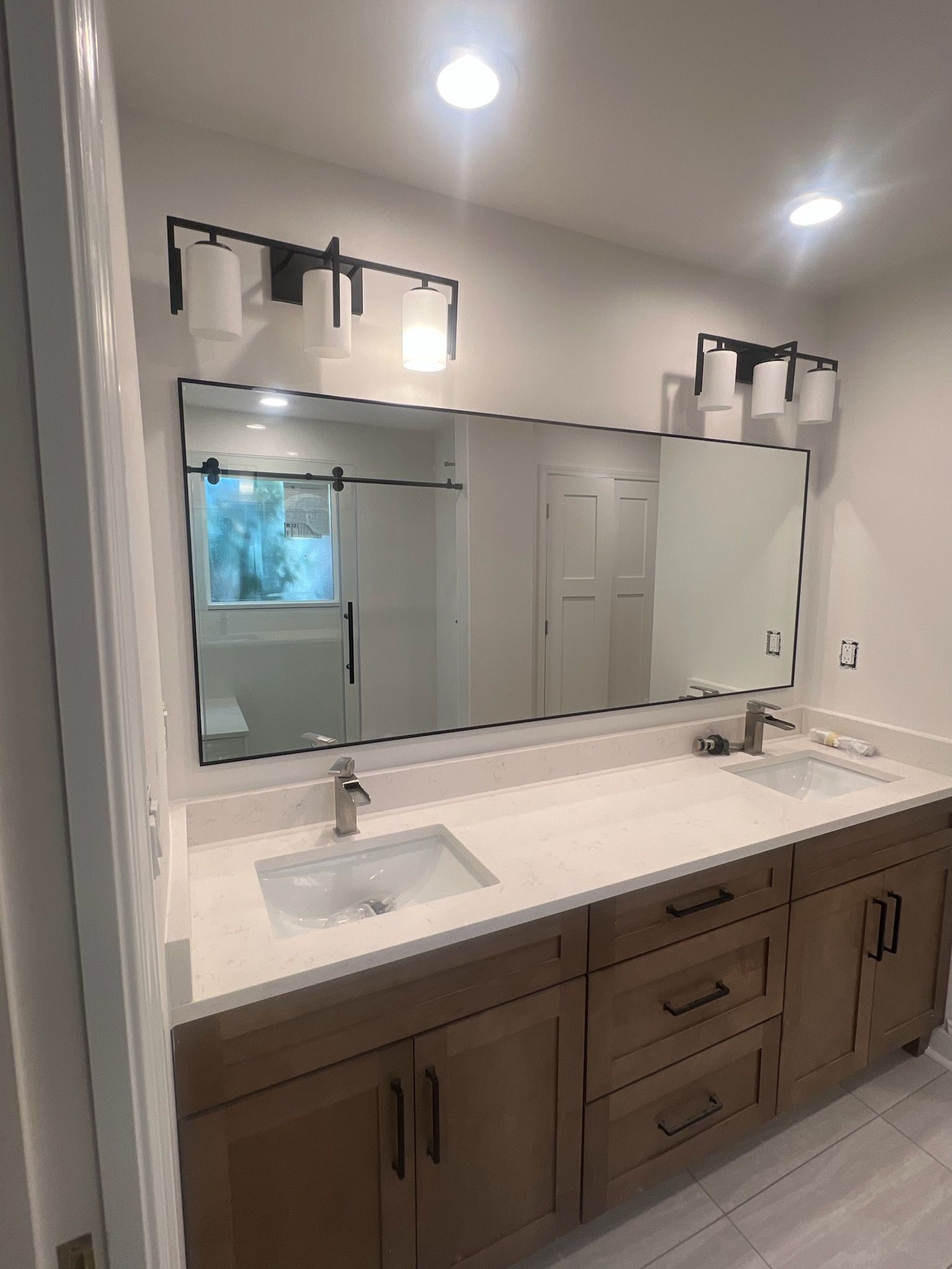 Bathroom with double vanity, large mirror, and black light fixtures. Wooden cabinets and light countertop.