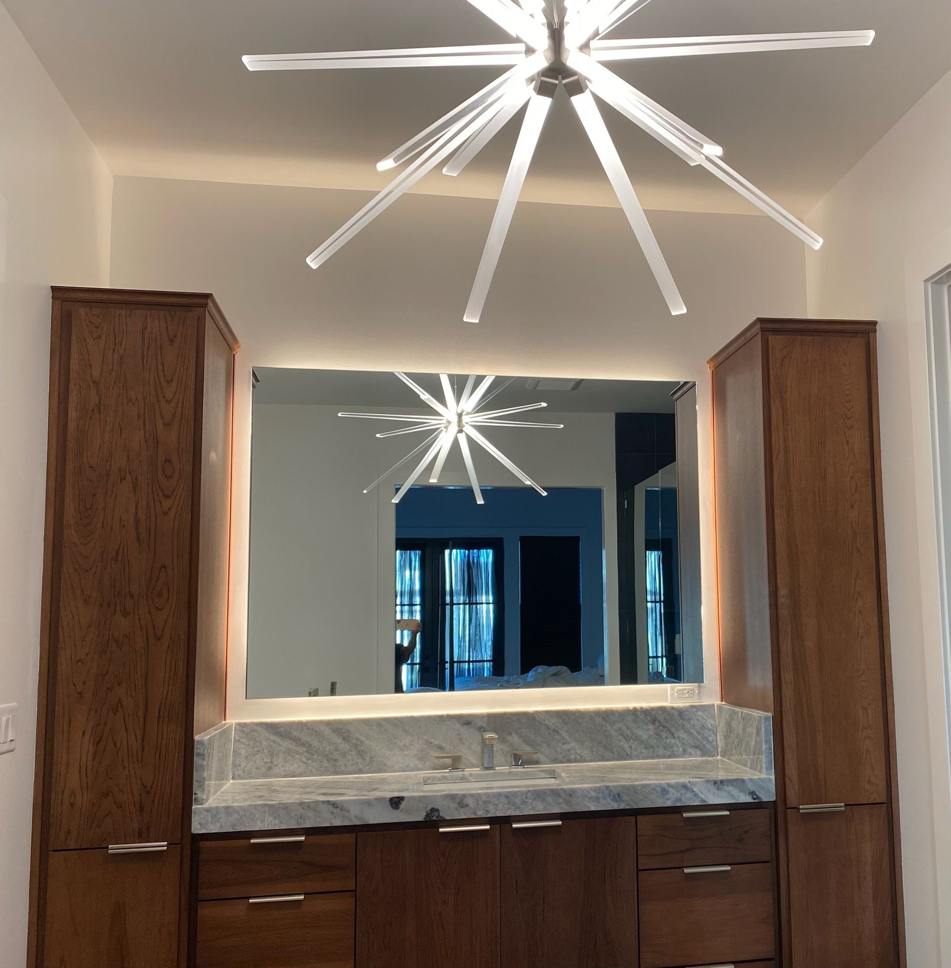 Wooden bar with cabinets, granite countertop, large mirror, and starburst light fixture.