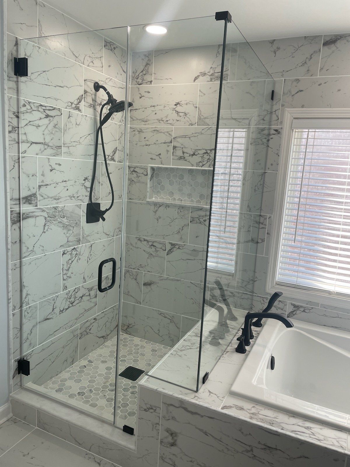 Glass shower enclosure with black fixtures in a bathroom with marble-look tile.