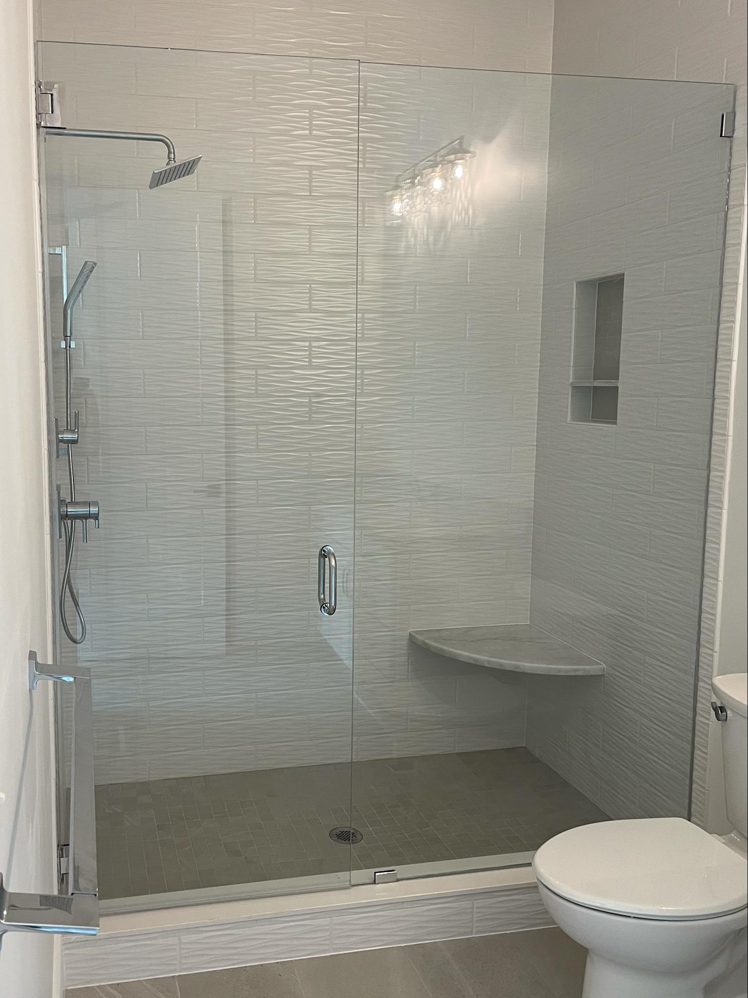Modern bathroom with clear glass shower, textured white tiles, and a built-in seat.