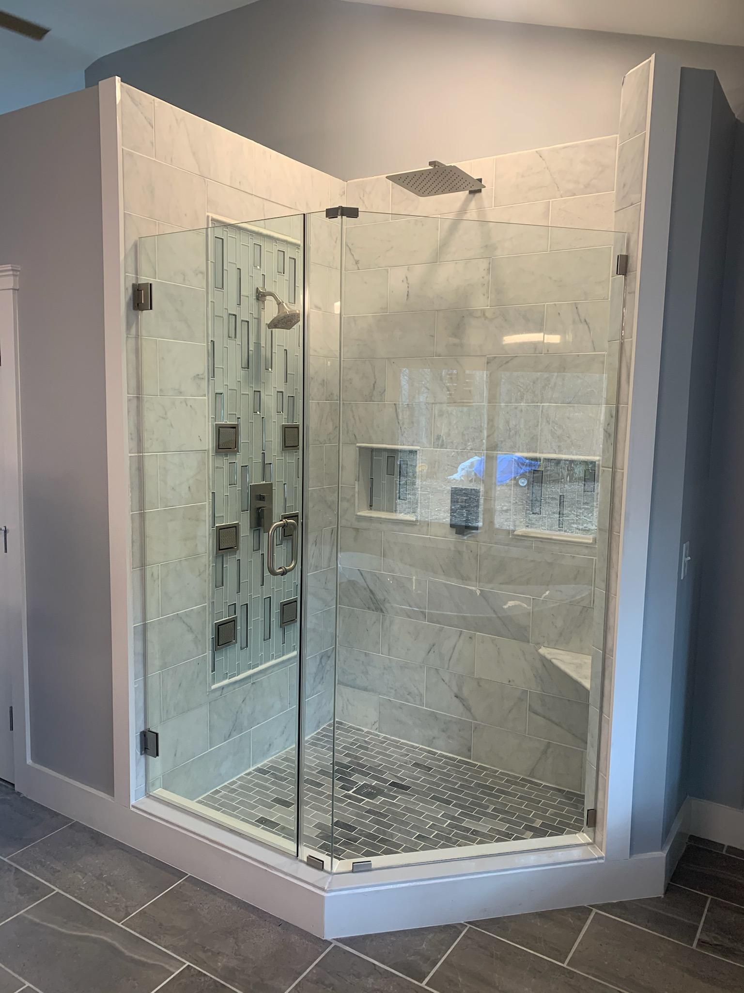 Corner glass shower with marble tile walls and floor.