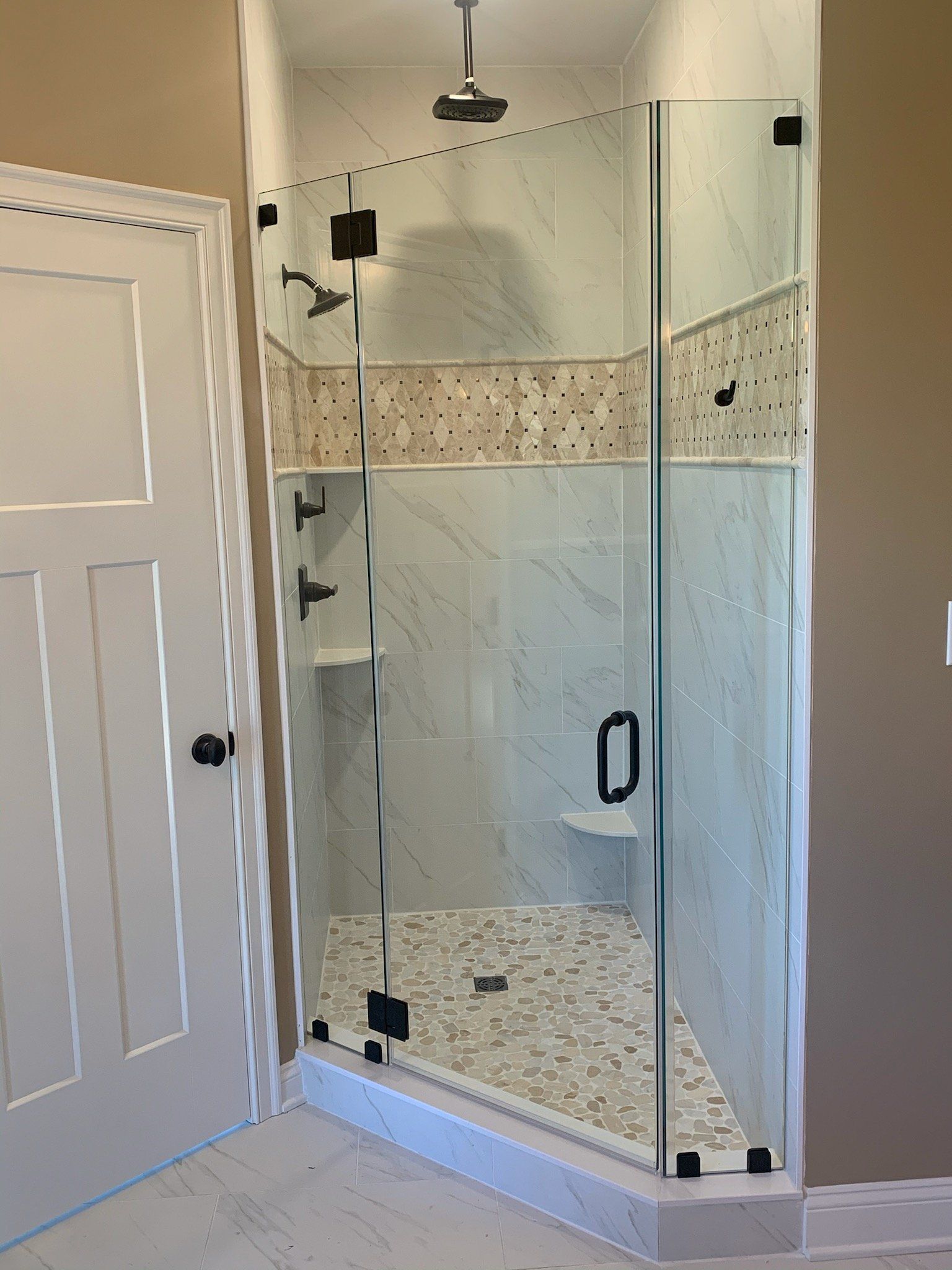Glass shower enclosure with black hardware and pebble floor.