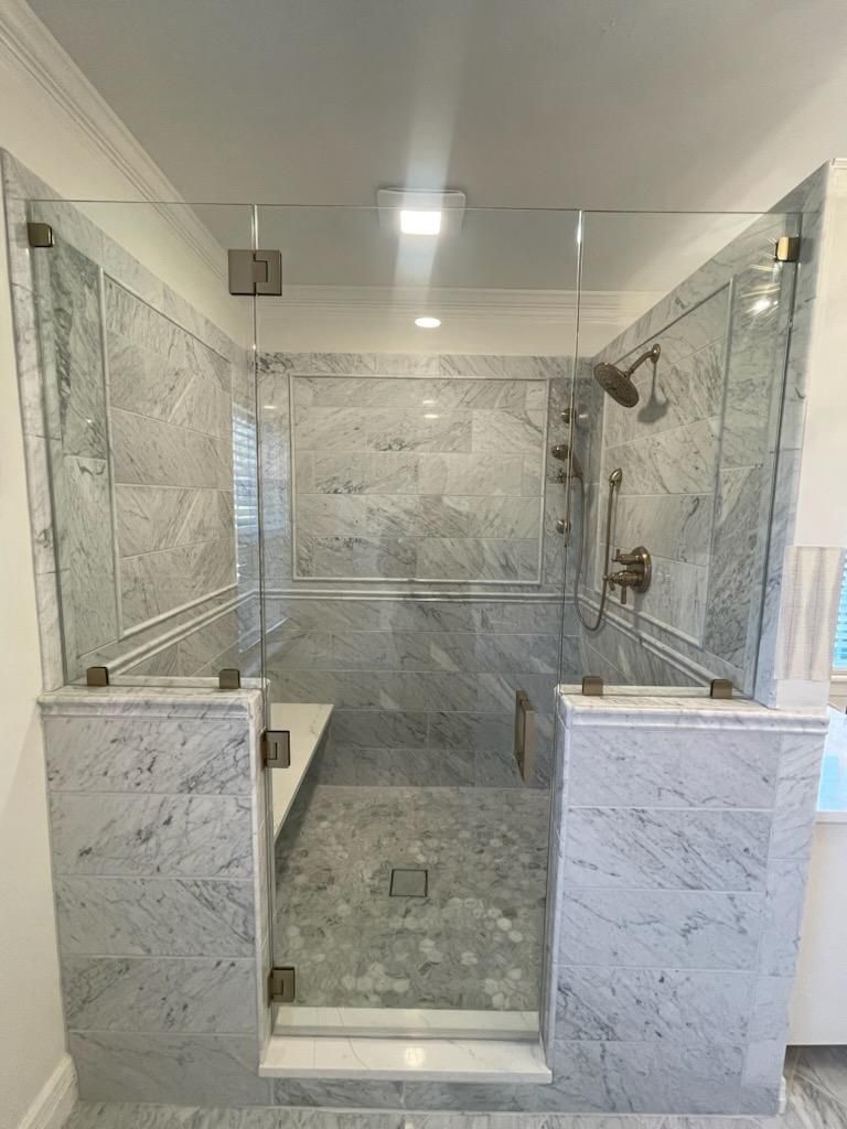 Glass shower enclosure with marble tile walls and brass fixtures.