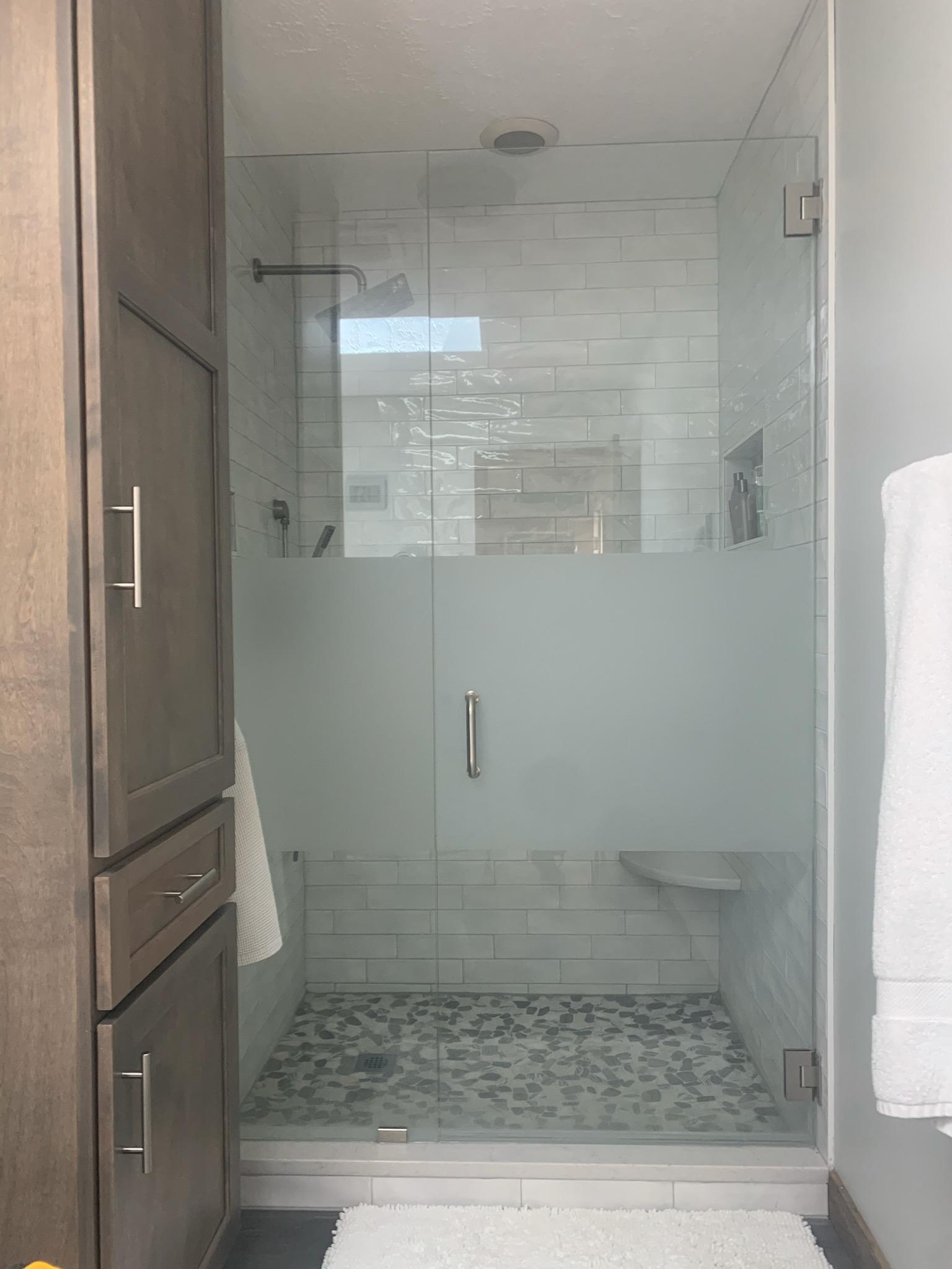 Bathroom with a frosted glass shower, gray cabinets, and a white rug.