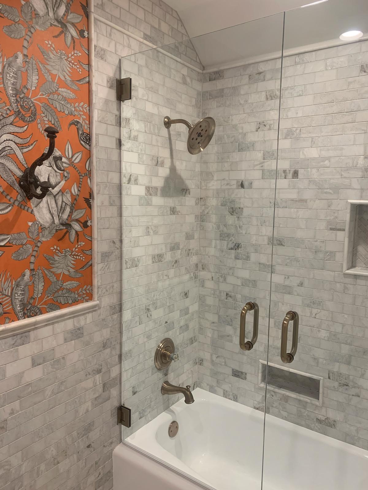 Bathroom with a glass shower, marble tile, and an orange floral art piece.