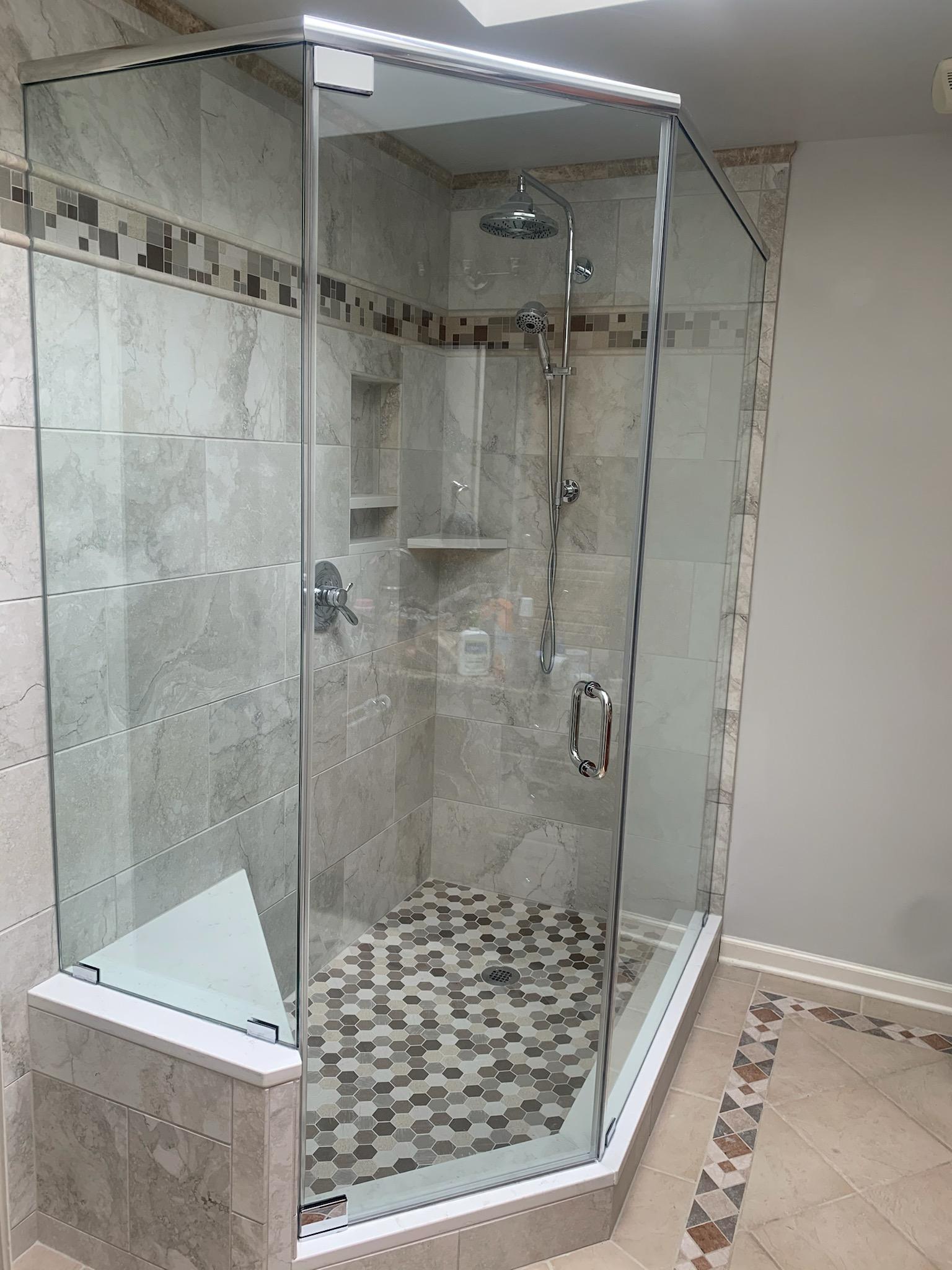 Corner shower with glass doors, tiled walls, and a stone mosaic floor.