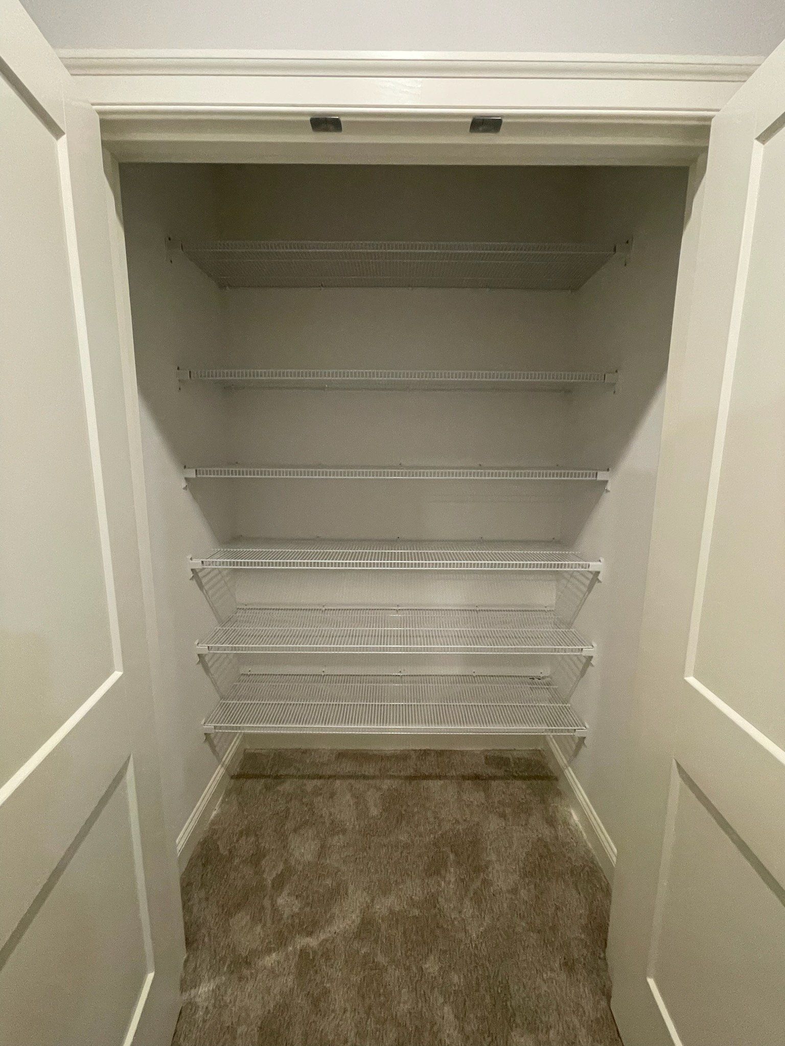 Empty white closet with wire shelves, neutral carpet.