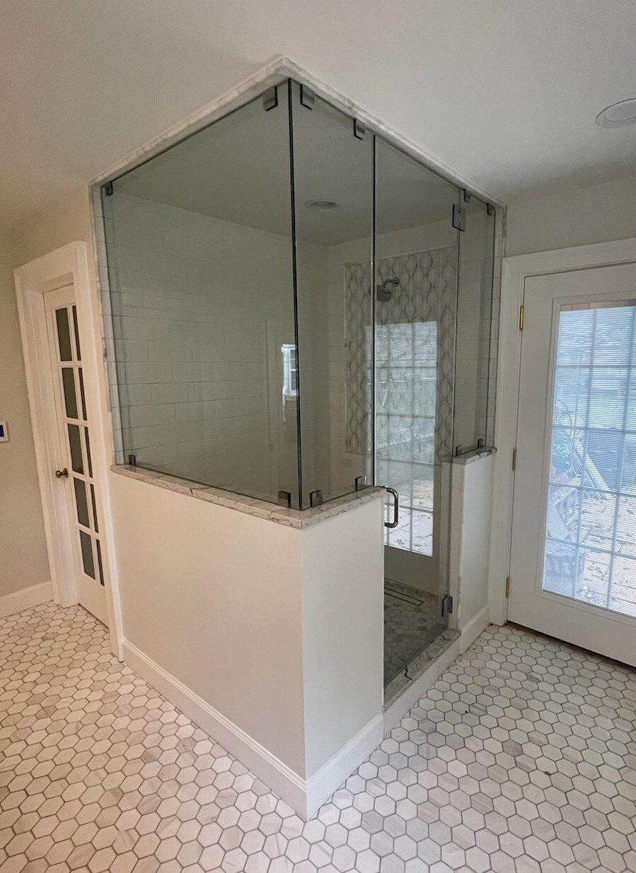 Glass shower enclosure in a bathroom with white and gray tile flooring.