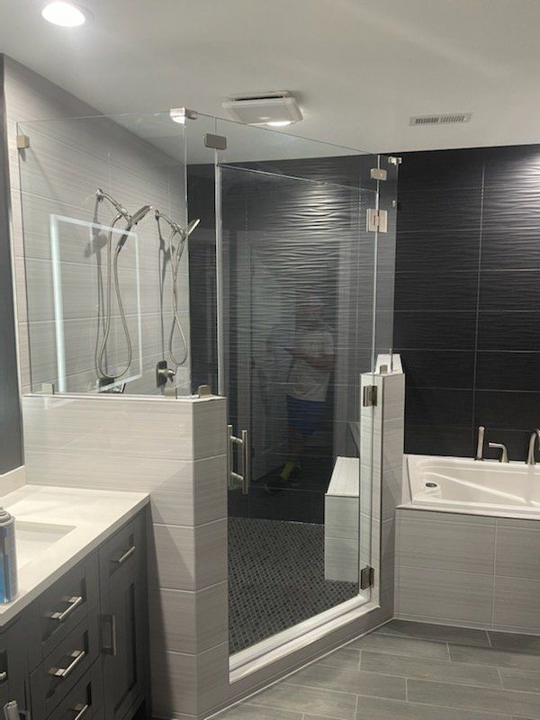 Modern bathroom with glass shower, gray tile, black accent wall, and a vanity.