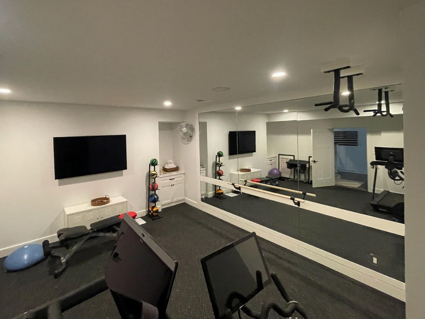 Home gym with workout equipment: treadmill, weights, mirrors, and TVs.