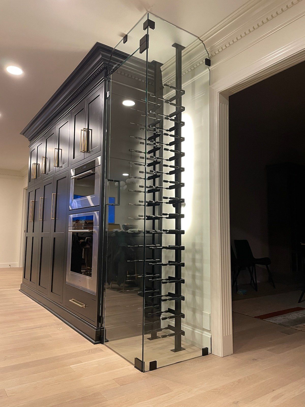 A luxury home wine cellar with a black cabinet, glass wine rack, and light wood floors.