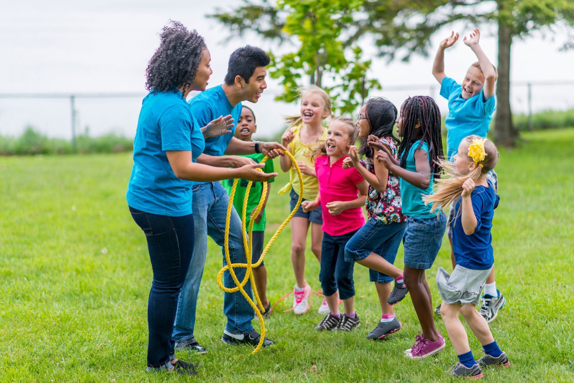 Children and two adults playing tug-of-war with a rope outdoors on a grassy field