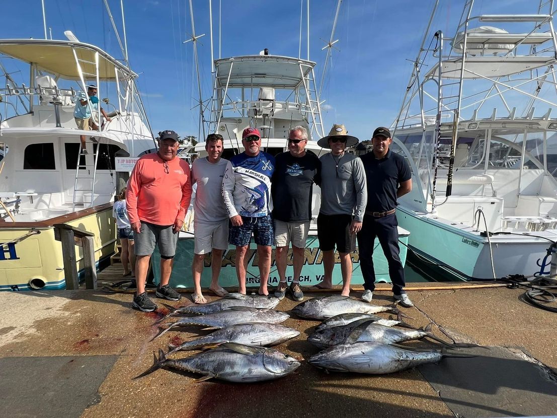 A group of men standing next to a pile of fish on a dock.