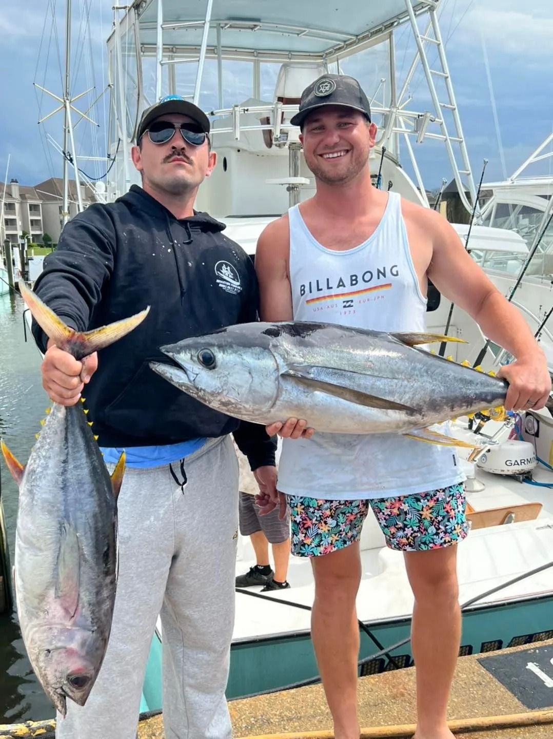 Two men are holding large fish in front of a boat.