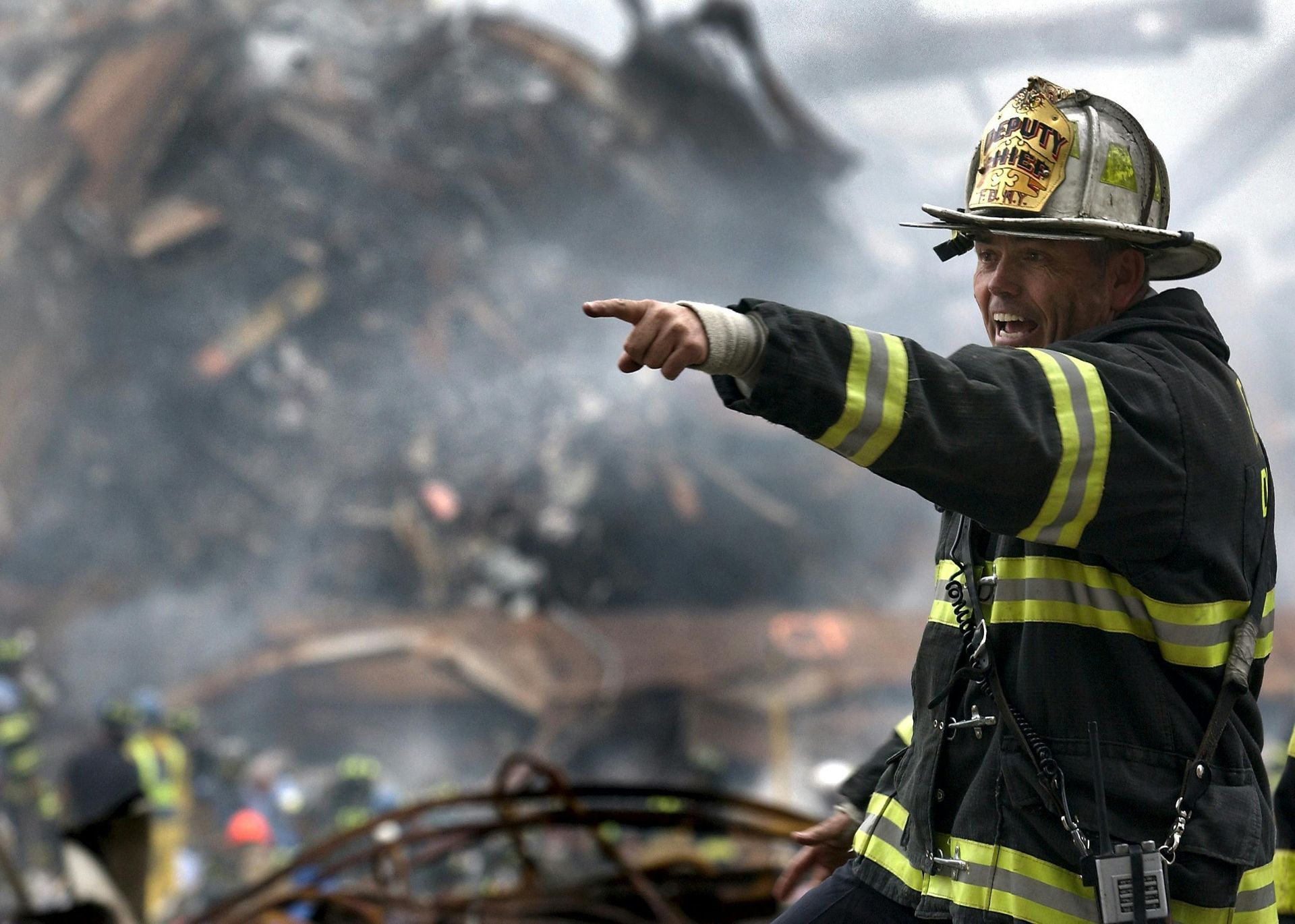 Firefighter points towards debris, smoke billowing, after 9/11 attacks.