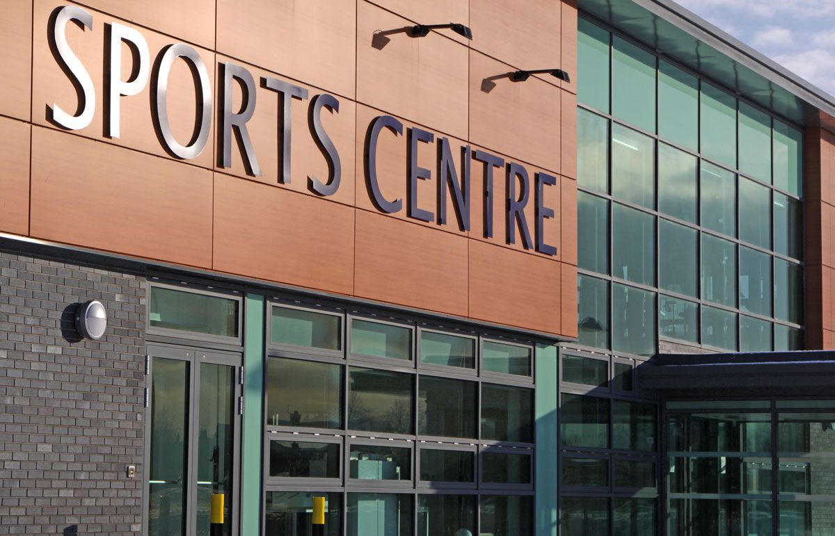 Sports Centre building with large SPORTS CENTRE sign. Exterior shot with glass and brown panels.