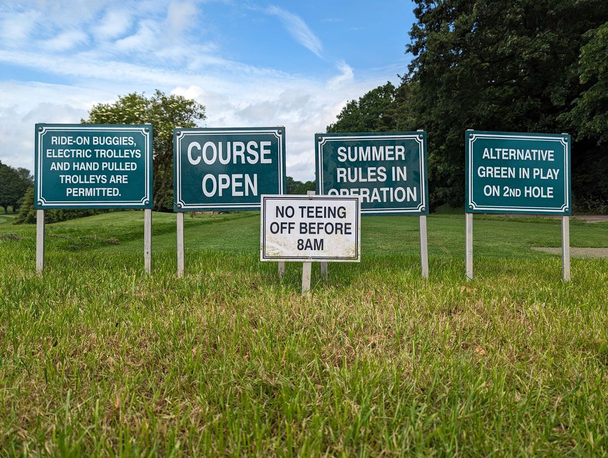 Signs on a golf course: electric trolleys permitted, course open, summer rules in operation, alternating green in play on 3rd hole, no teeing off before 8 AM.