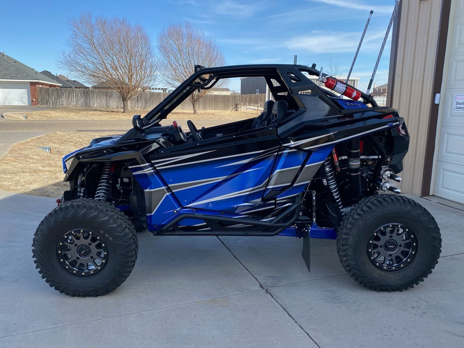 Blue and black off-road vehicle with large tires parked outside, sunny day.