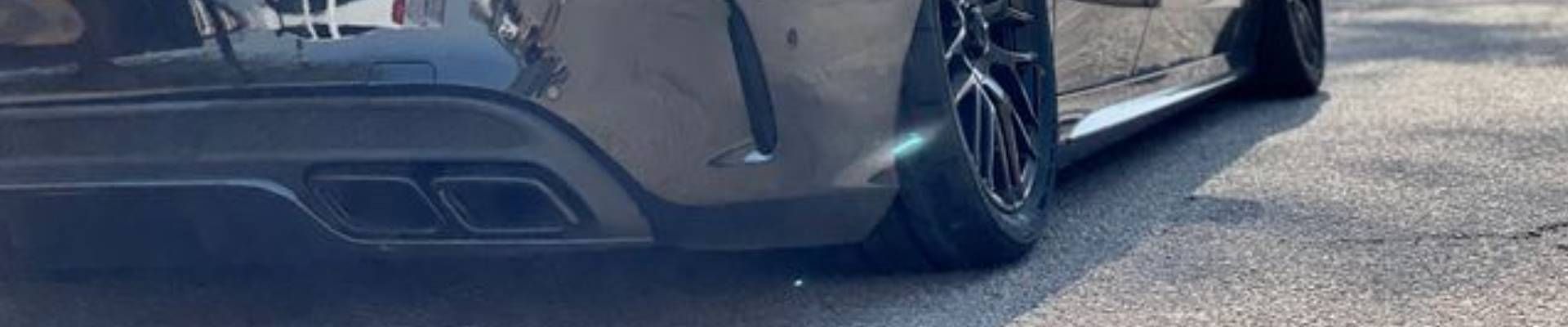 Black car's rear, with two exhaust pipes, black wheels, and asphalt surface.