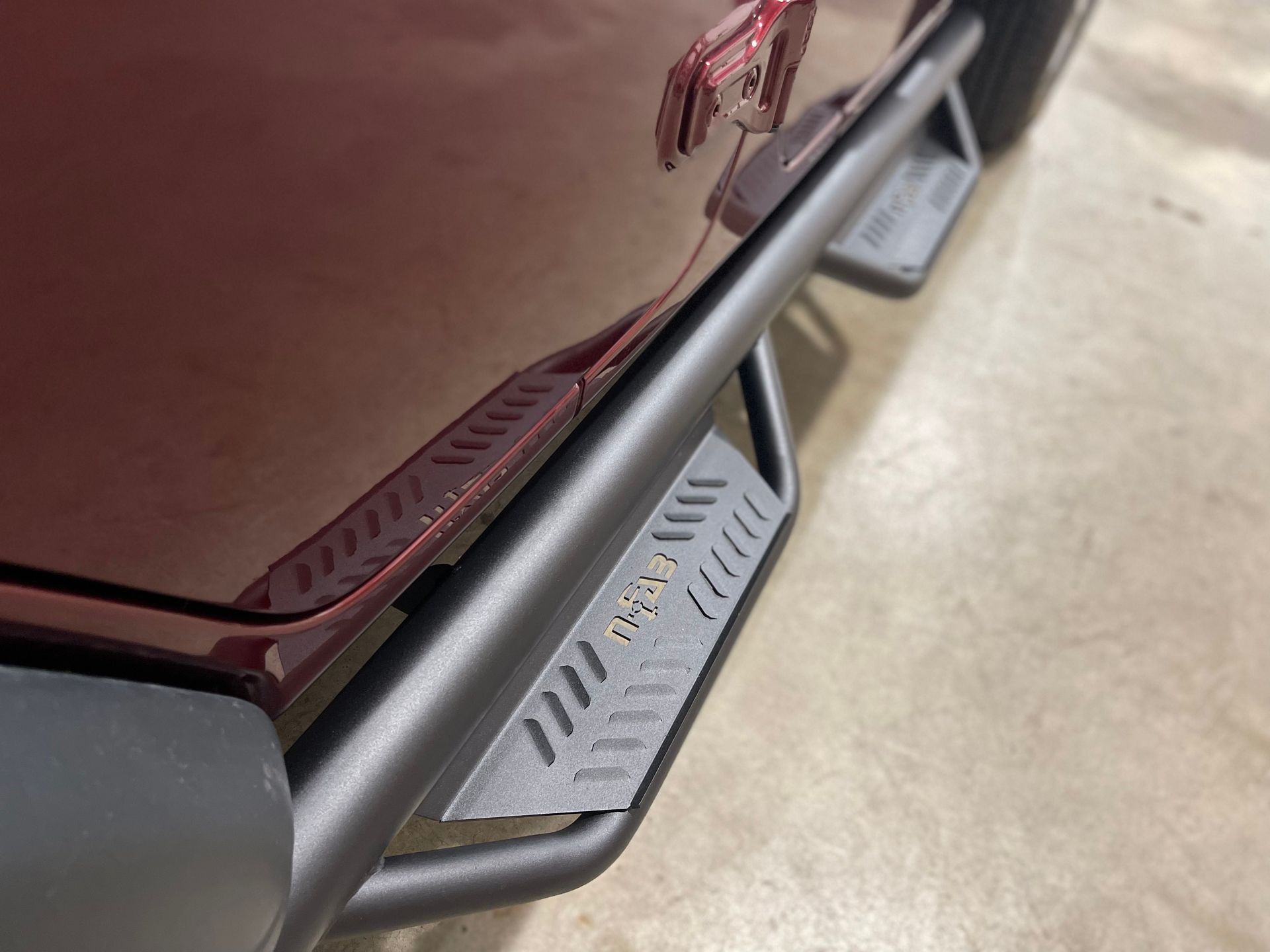 Black running board attached to a red vehicle, with integrated step.