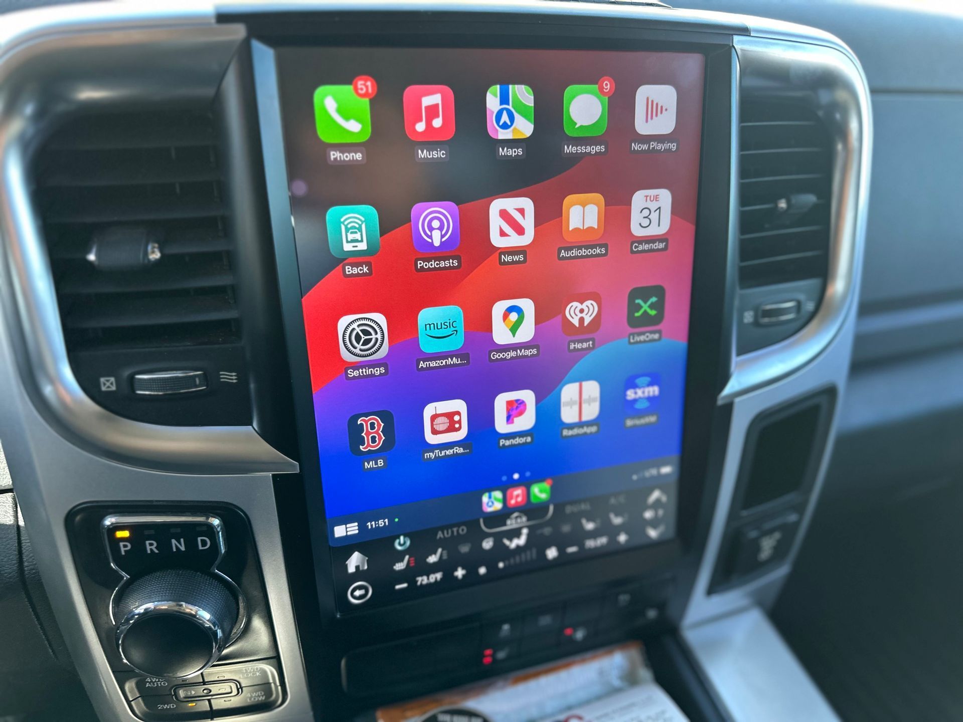 Large touchscreen display in a car's dashboard, displaying app icons. The car interior is visible.