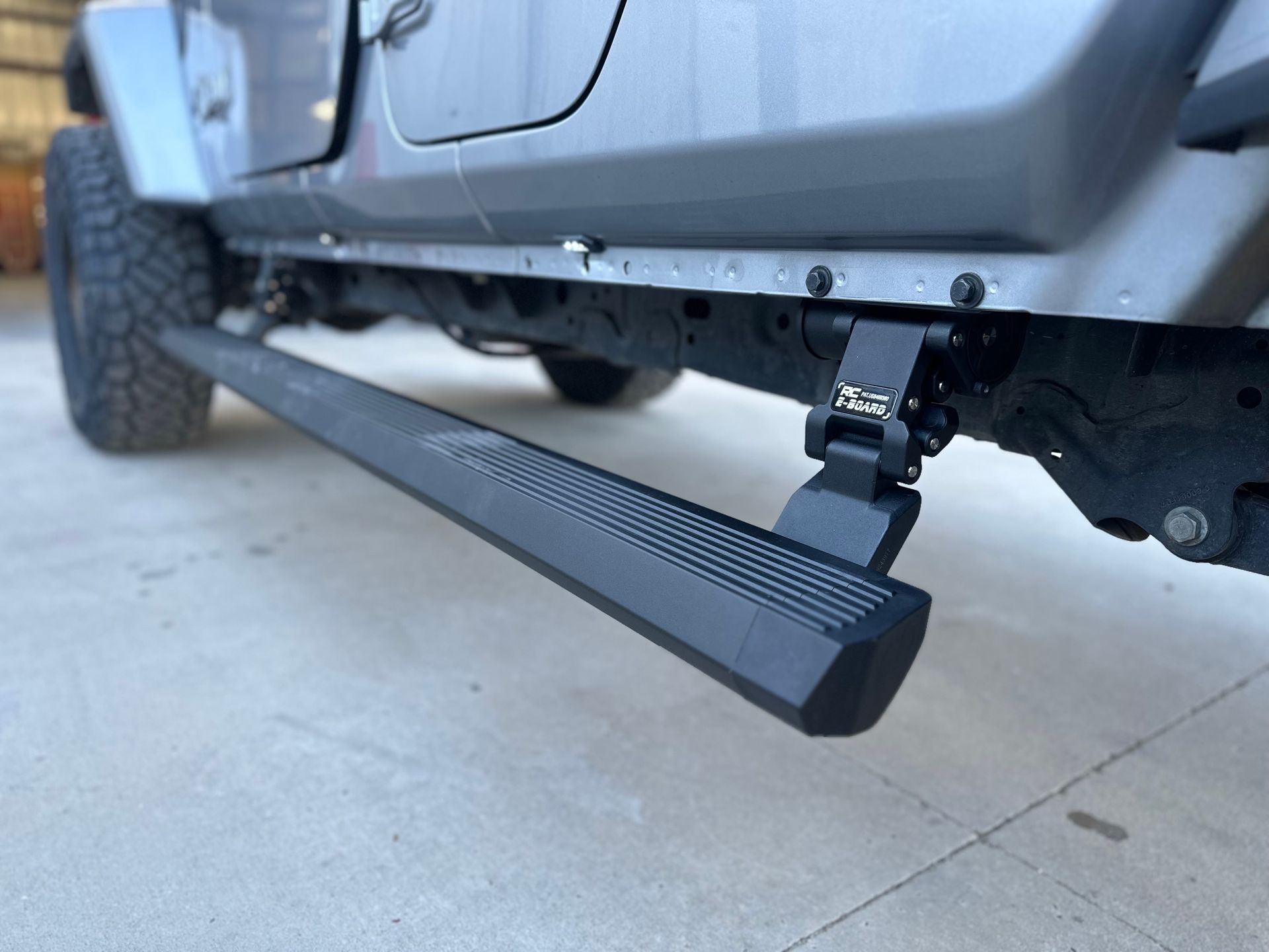Gray Jeep with a black, retractable running board on a concrete surface.