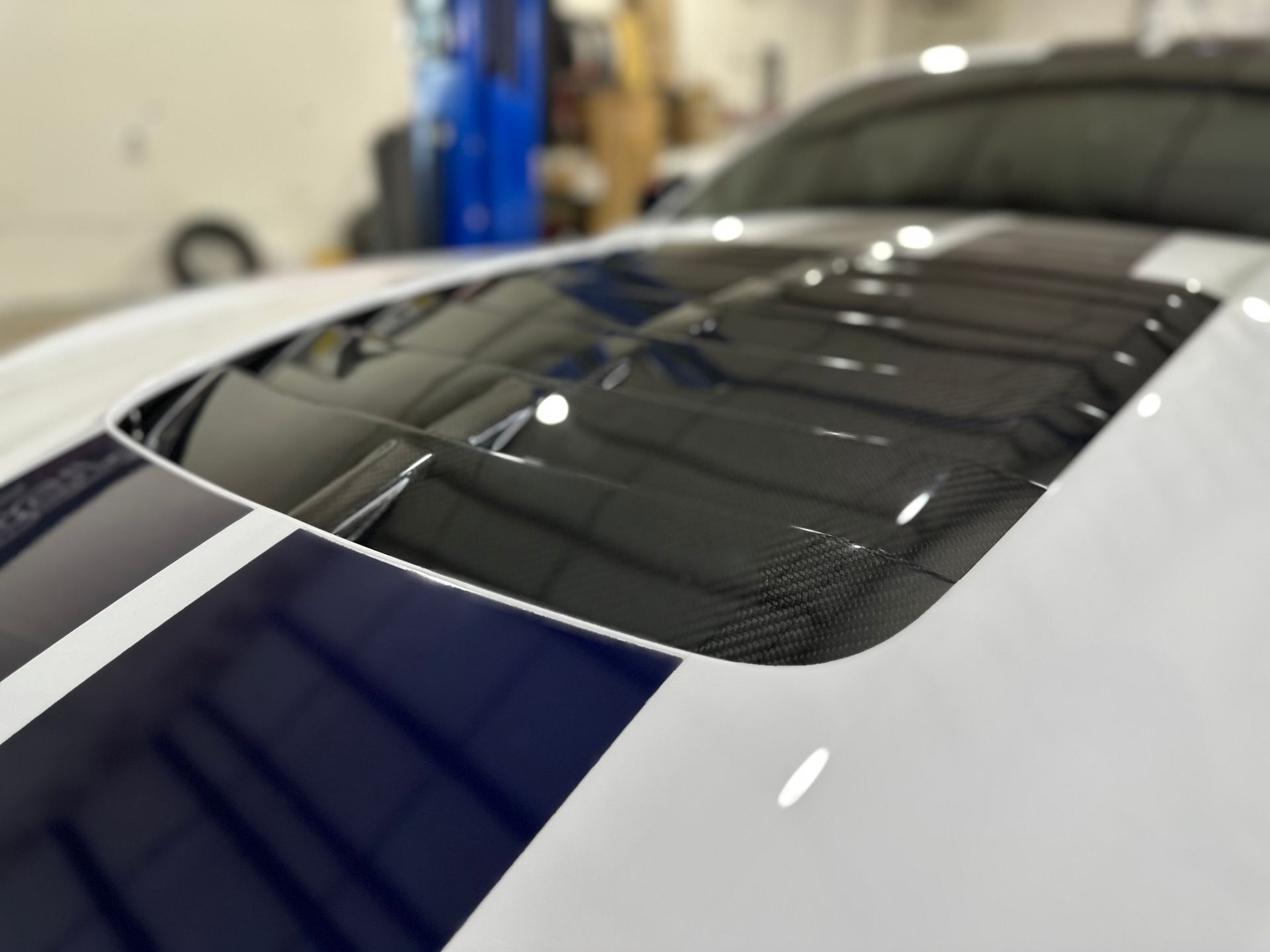 White car hood with blue racing stripe and carbon fiber hood vent.