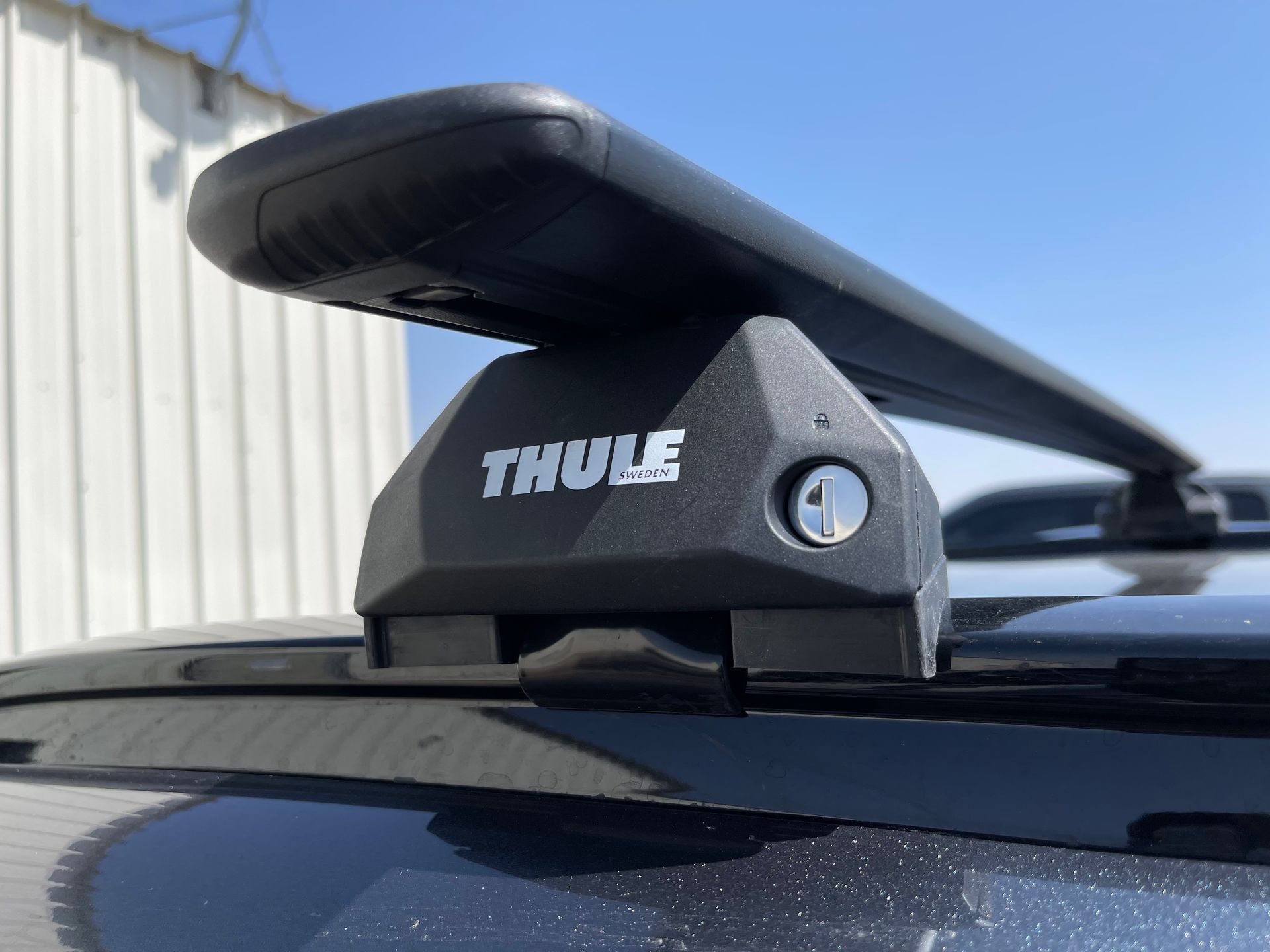 Black Thule roof rack attached to a dark-colored vehicle, outdoors with a bright sky in the background.