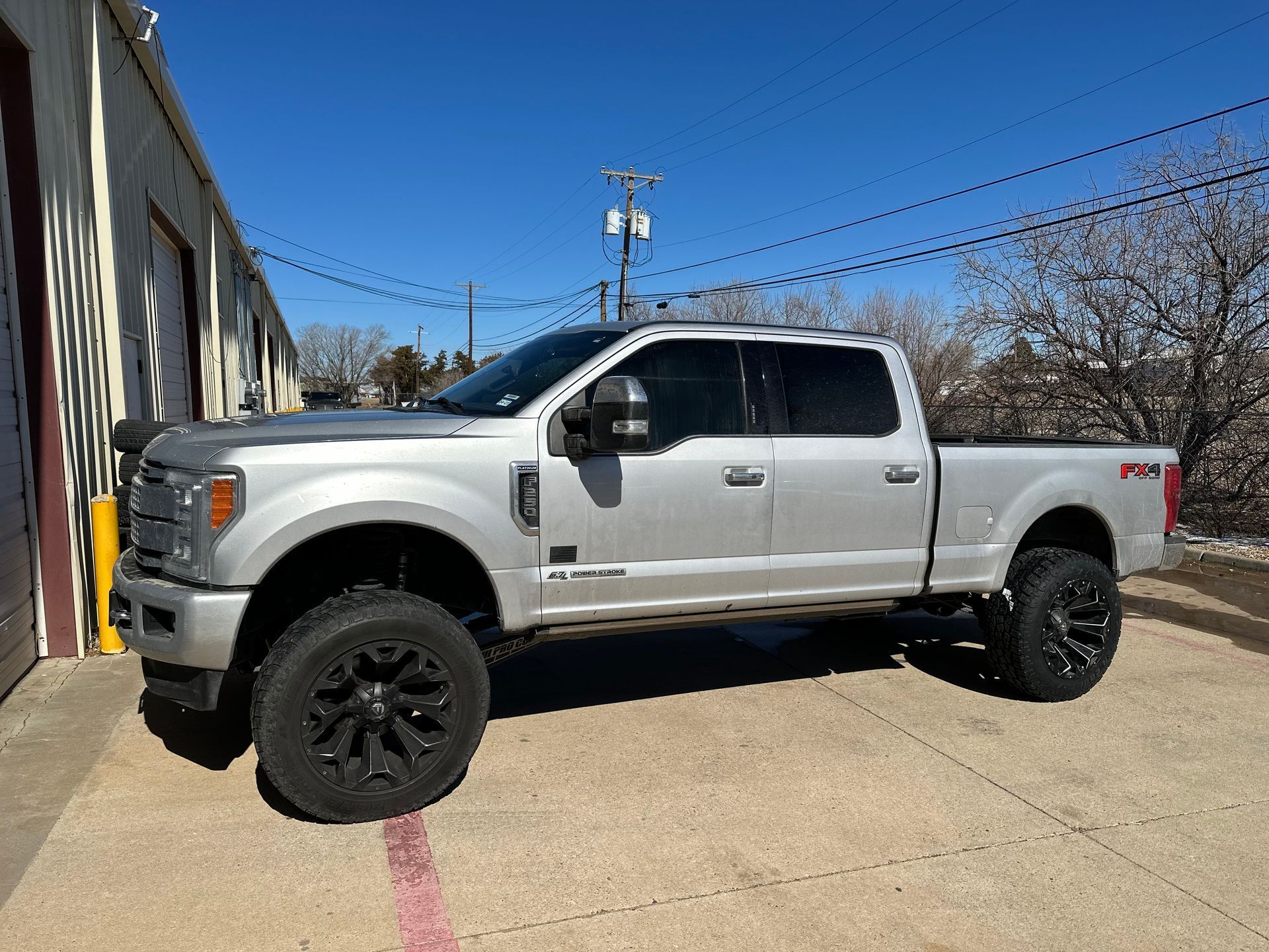 Silver lifted Ford truck parked in front of a building on a sunny day.