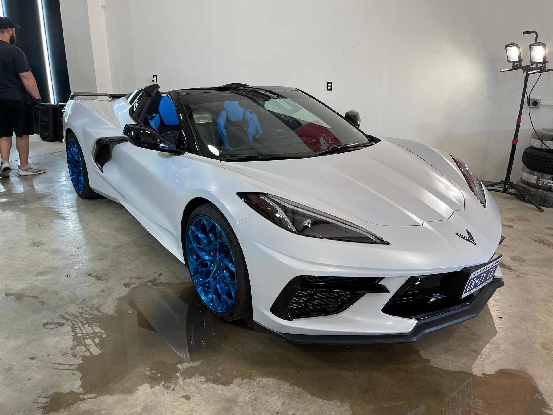 White Corvette with blue wheels, convertible top down, parked indoors.