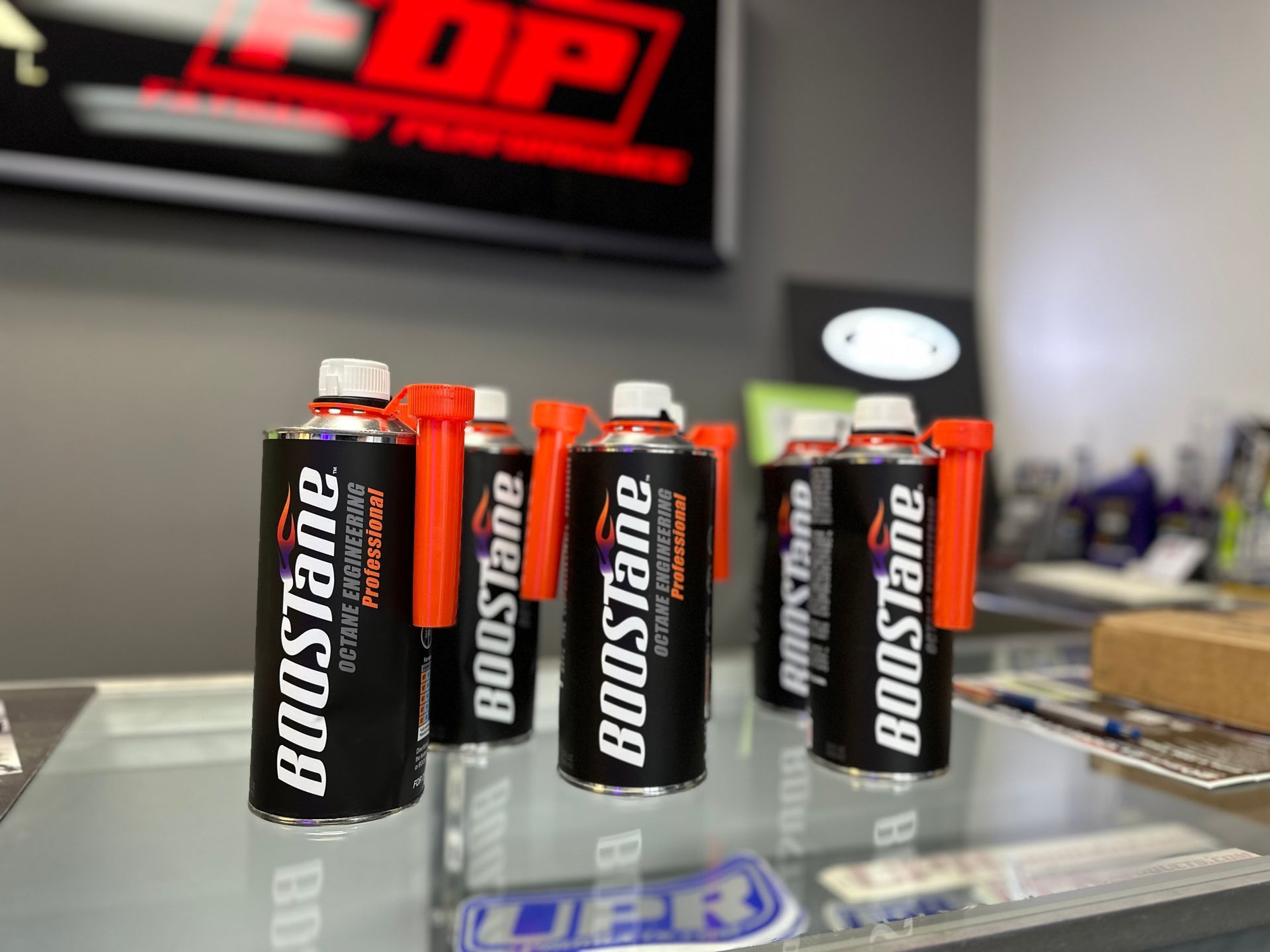 Boostane fuel additive cans with orange caps, arranged on a glass surface in a store.