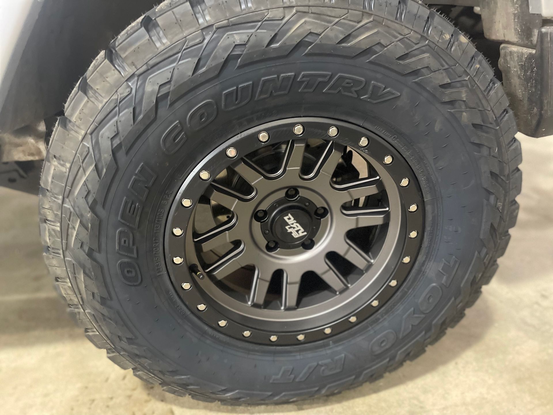 Black and gray off-road tire on a dark gray rim with visible bolt heads.